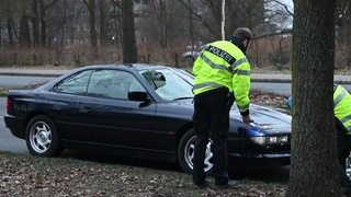 Ein Unfallwagen mit kaputter Windschutzscheibe wird von Polizisten untersucht.