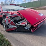 Ein kaputter roter Lamborghini steht am Rande der Autobahn.