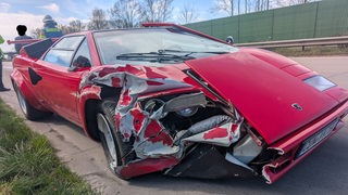 Ein kaputter roter Lamborghini steht am Rande der Autobahn.