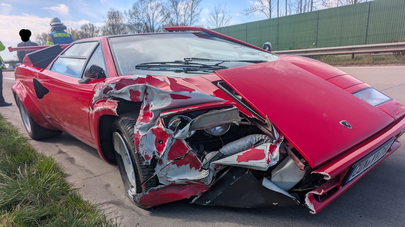 Ein kaputter roter Lamborghini steht am Rande der Autobahn.