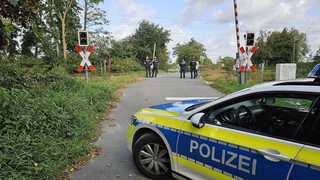Ein Polizeiauto steht vor einem Bahnübergang, die Schranken sind oben und Polizisten stehen vor den Gleisen.