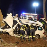 Ein vollkommen zerstörtes Auto liegt in einem Straßengraben. Feuerwehrleute versuchen Verletzte aus dem Auto zu retten.
