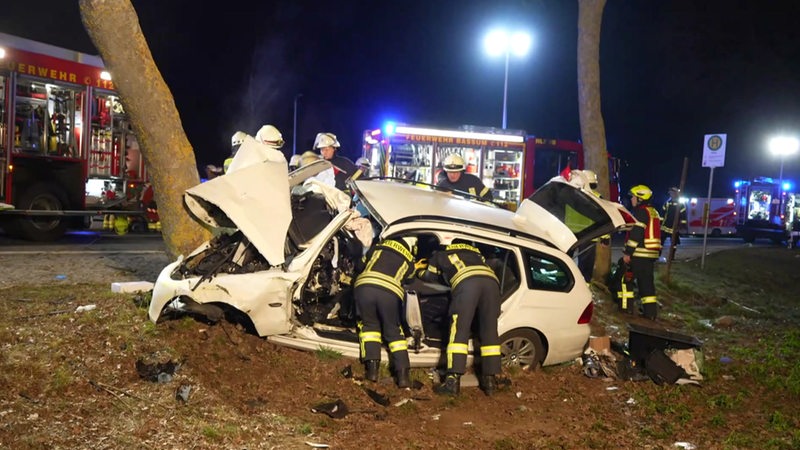 Ein vollkommen zerstörtes Auto liegt in einem Straßengraben. Feuerwehrleute versuchen Verletzte aus dem Auto zu retten.