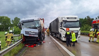 Nach einem Unfall auf der A1 laufen mehrere Feuerwehrleute zwischen zwei beschädigten Lastwagen umher.