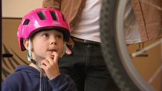 Ein vierjähriges Kind mit pinkem Helm schaut ein Fahrrad an.