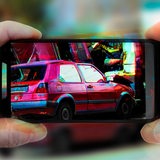 Zwei Hände halten ein Smartphone auf dem ein Unfallauto zu sehen ist.