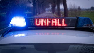 Ein Einsatzfahrzeug der Polizei mit Blaulicht und dem Schriftzug Unfall im Display, steht auf einer Landstraße.