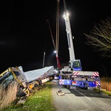 Ein Lkw liegt in einem Straßengraben und wird von einem Kran geborgen.