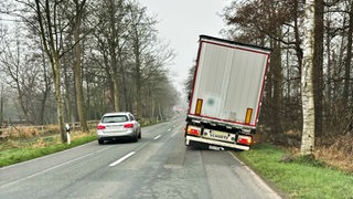 Ein Pkw umfährt einen am Straßenrand schiefstehenden Lkw.