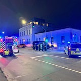 Ein Feuerwehr- und ein Polizeiauto stehen auf einer Kreuzung. Im Hintergrund steht ein Camper-Van an einer Hauswand.