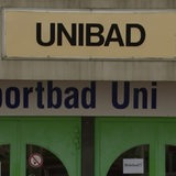 Zwei grüne Doppeltüren sind zu sehen. Darüber ein Banner auf dem steht Sportbad Uni und links daneben das blaue Logo der Bremer Bäder.