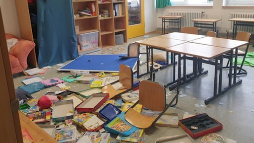 Ein verwüstetes Klassenzimmer mit Stühlen, Spielen und Büchern durcheinander auf dem Boden liegend. 