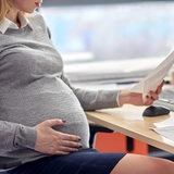 Eine schwangere Frau sitzt in einem Büro und schaut sich Unterlagen an. (Symbolbild)