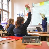 Schüler sitzen im Unterricht und zeigen auf