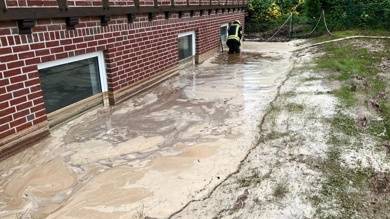 Ein Feuerwehrmann pumpt Regenwasser aus der Grube vor einem Wohnhaus. 