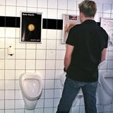 Ein Mann steht vor einem Urinal in einer Männer-Toilette.