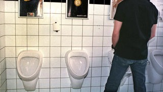 Ein Mann steht vor einem Urinal in einer Männer-Toilette.