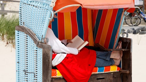 Eine Urlauberin liegt im Strandkorb und liest ein Buch