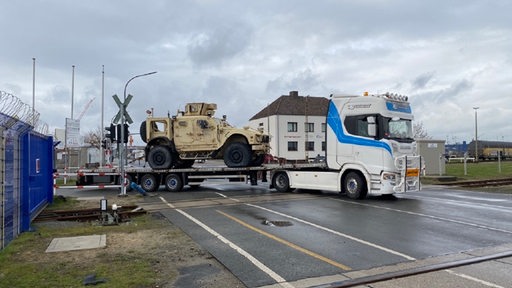 Ein Lkw mit einem Militärfahrzeug fährt über einen Bahnübergang.