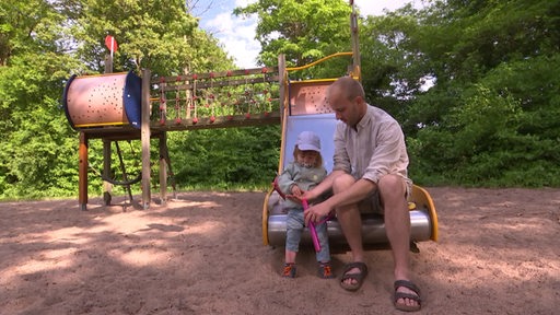 Ein Vater mit seinem Kind auf sitzen auf einer Rutsche auf einem Spielplatz.