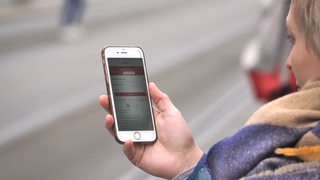 Eine Frau nutzt die VBN-App "Fahrplaner" an einer Straßenbahnhaltestelle.