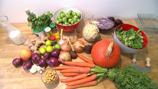 Diverse Gemüsesorten wie Rosenkohl, Karotten und Zwiebeln auf einem Tisch.