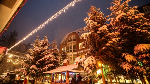 Eine Lichterkette ist über den Vegesacker Weihnachtsmarkt gespannt.Auf den Bäumen und Dächern liegt Schnee.