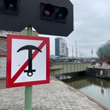 Ein Schild mit einem durchgestrichenen Anker ist im Vordergrund zu sehen. Im Hintergrund ist eine Brücke über einen Kanal zu sehen sowie das Klimahaus und Hochhäuser.