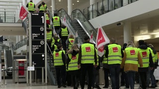 Mitglieder der Gewerkschaft Verdi streiken am Bremer Flughafen. Die Mitarbeiterinnen tragen gelbe Warnwesten und schwenken Fahnen.