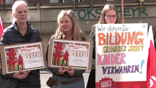 Erzieherinnen protestieren gegen die Kita-Pläne mithilfe von Plakaten