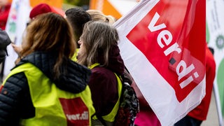 Streikende in Warnwesten halten eine Verdi-Fahne hoch.