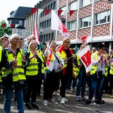 Menschen mit gelben Warnwesten und Fahnen mit der Aufschrift "Verdi" stehen in einer Fußgängerzone.