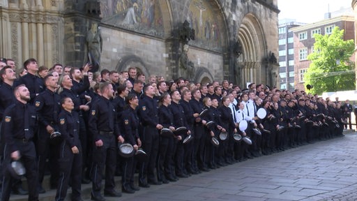 Der neue Ausbildungsjahrgang der Bremer Polizei steht für ein Gruppenfoto beieinander und ist im Begriff ihre Mützen in die Höhe zu werfen. 