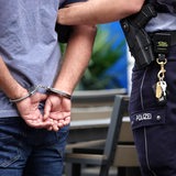Ein Mann steht in Handschellen neben einem Polizisten.