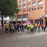 Menschen in gelben Warnwesten stehen vor einem Gebäude.