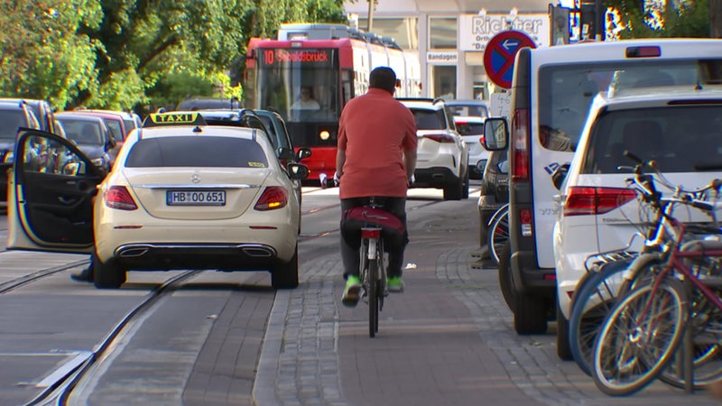 Eine von einem Fahrradfahrer, mehreren Autos und einer Straßenbahn befahrene Straße.