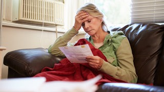 Eine Seniorin blickt sorgenvoll auf eine Rechnung.