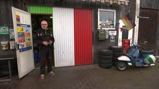Karl Heinz Grunert steht vor seiner Werkstatt mit grün-weißen-rotem Anstrich