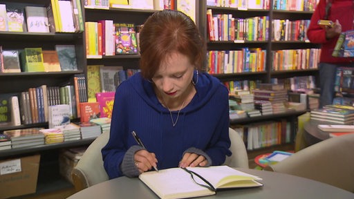 Vivien Altenau in einer Buchhandlung. Sie schreibt in einem Buch.