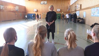 Laura Ludwig spricht in der Turnhalle mit jungen Schülerinnen und Schülern.