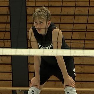 Ein Jugendlicher steht hinter einem Volleyballnetz.