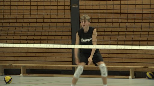 Ein junger Volleyballer steht mit gebeugten Knien beim Training in der Turnhalle hinter dem Netz