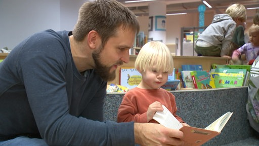 Ein Vater liest einem Kind aus einem Buch vor.