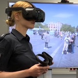 Eine Polizistin steht vor einem Bildschirm und trägt eine VR-Brille und Controller
