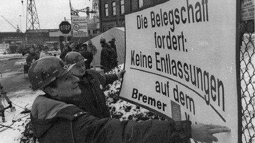 Arbeiter befestigen am 20. Februar 1996 ein Protestplakat am Werkstor in Bremen-Nord. Vor dem Eingang der von der Schliessung bedrohten Vulkan-Werft ist eine Mahnwache von Arbeitern und Angestellten aufgezogen.