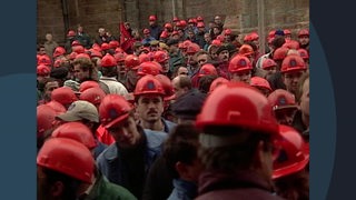 Mitarbeiter der Vulkan Werft protestieren gegen die geplante Schließung im Jahr 1996. Sie alle tragen rote Bauhelme mit dem Firmenlogo drauf. 