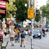 Ein Schild im Bremer Viertel zeigt die Waffenverbotszone an, im Hintergrund ist das Treiben im Viertel zu sehen.