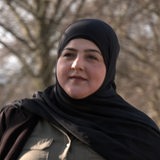 Eine Frau mit einem Kopftuch geht die Straße entlang.