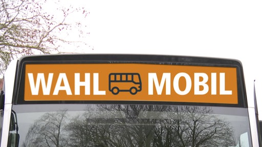 Auf dem Anzeigeschild eines Busses steht auf orangem Hintergrund "Wahl-Mobil".
