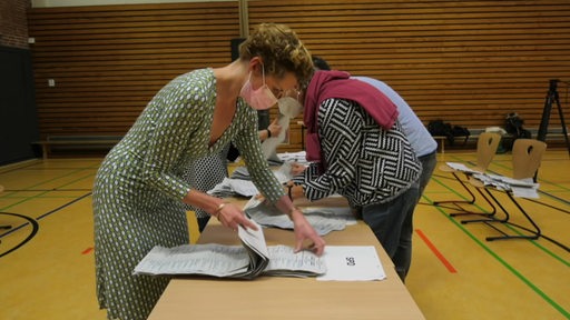 Eine Frau steht an einem Tisch und zählt Stimmzettel aus.